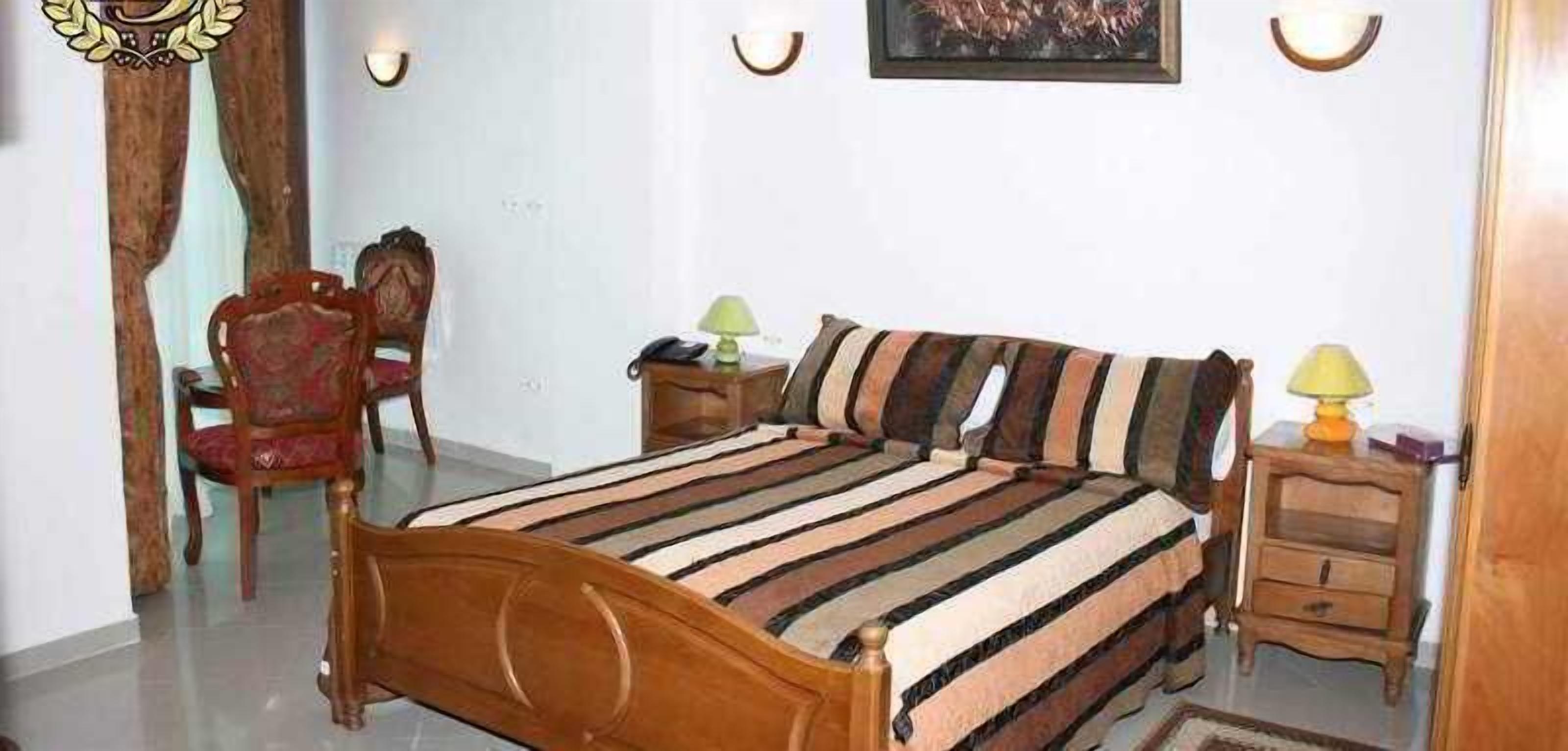 Een slaapkamer met een houten bed, een stoel, een nachtkastje en een wandlamp.