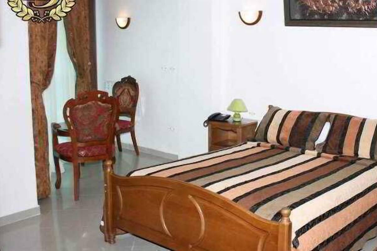 Een slaapkamer met een houten bed, een stoel, een nachtkastje en een wandlamp.
