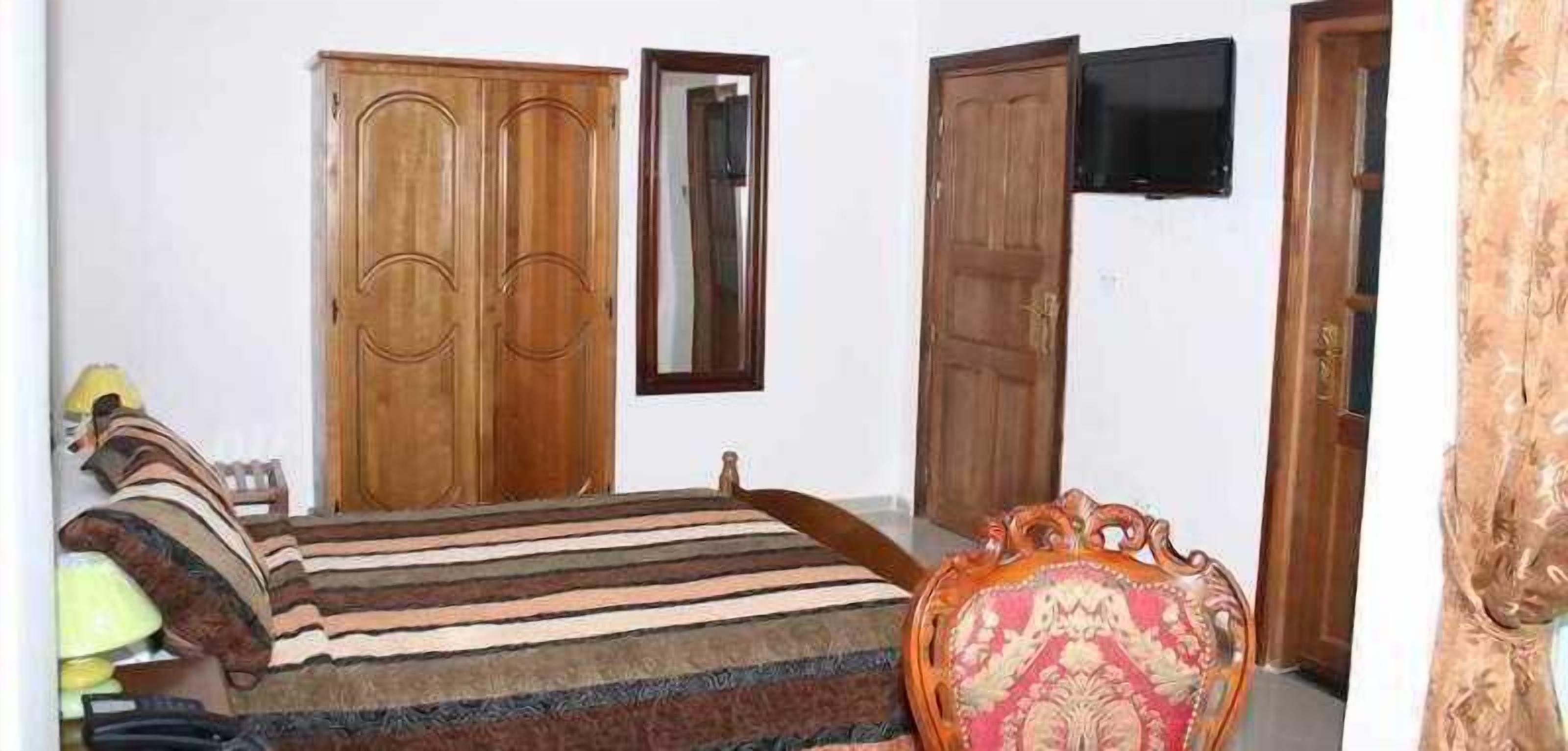 Een slaapkamer met een bed, een kledingkast, een televisie en een stoel.