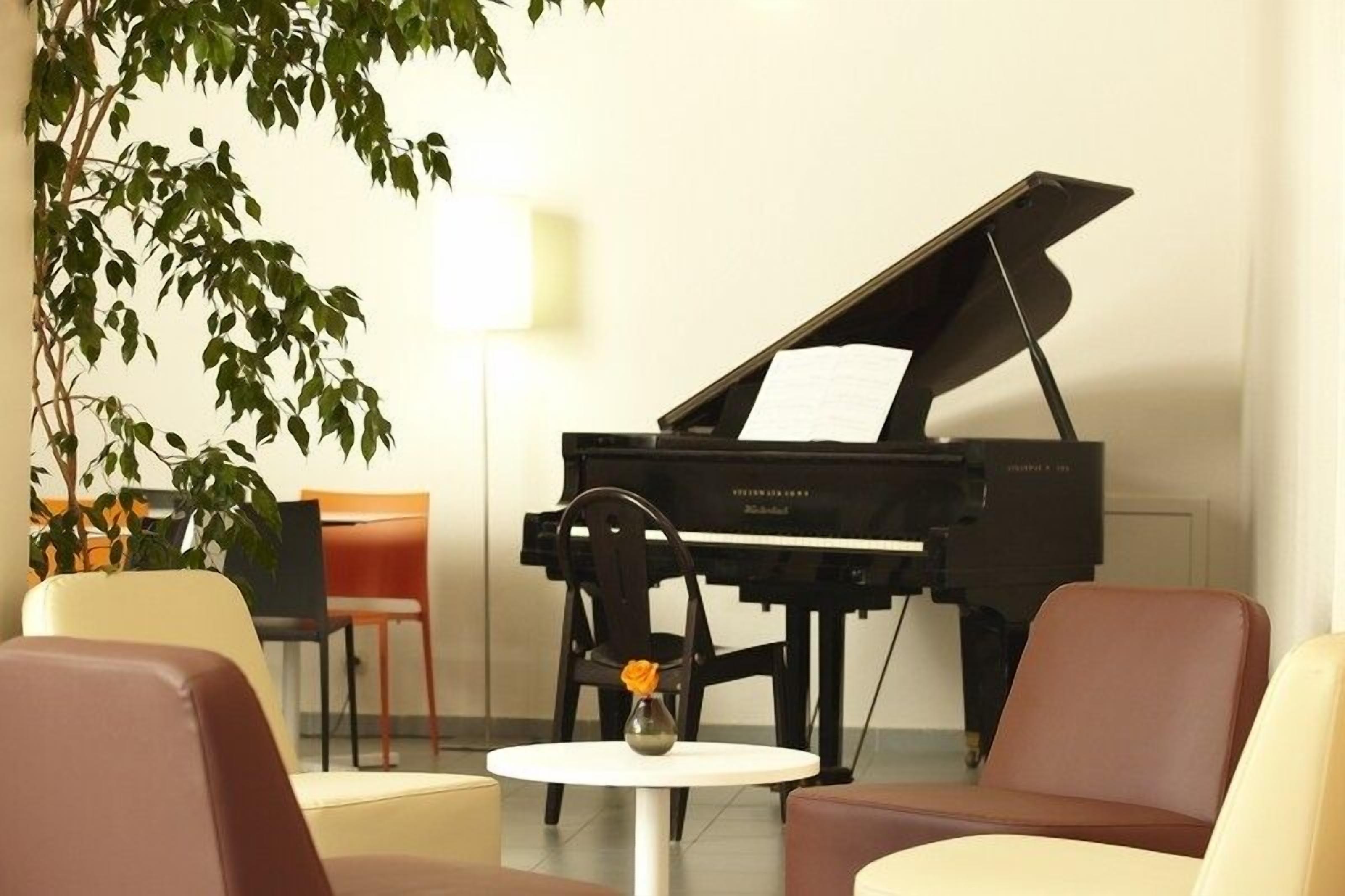 Un piano à queue dans une pièce meublée dans un style moderne, avec notamment une table ronde ornée d’un vase et une chaise.