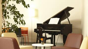Un piano à queue dans une pièce meublée dans un style moderne, avec notamment une table ronde ornée d’un vase et une chaise.