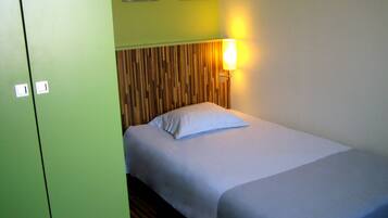 A single bed with a wooden headboard, a bedside lamp, and a green wall with two small pictures.