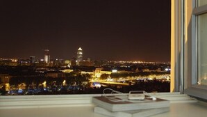 Vista nocturna desde una ventana con vistas a un paisaje urbano con edificios iluminados y una torre destacada.