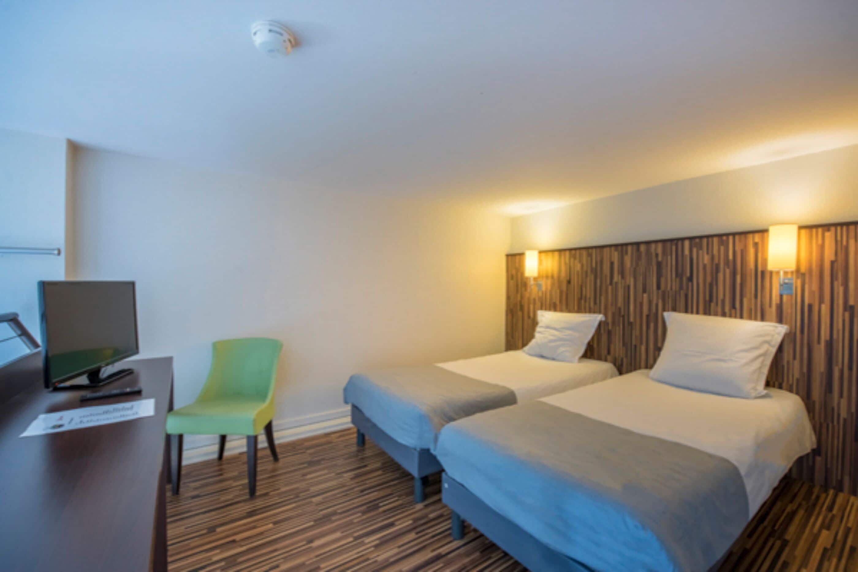 Habitación de hotel con dos camas, un escritorio con computadora, una silla y un panel de pared de madera.