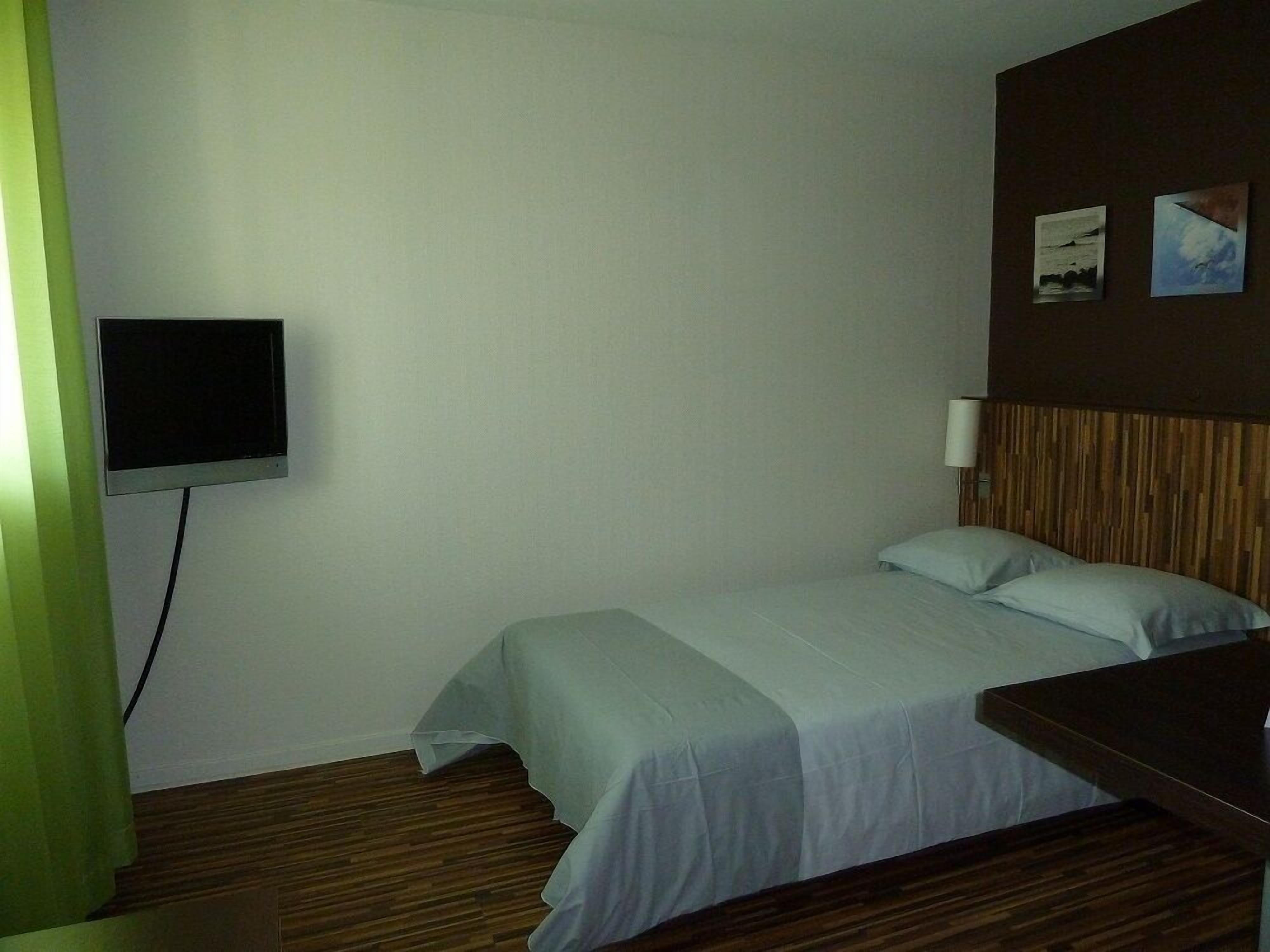A hotel room with a bed, a TV mounted on the wall, and a wooden headboard.