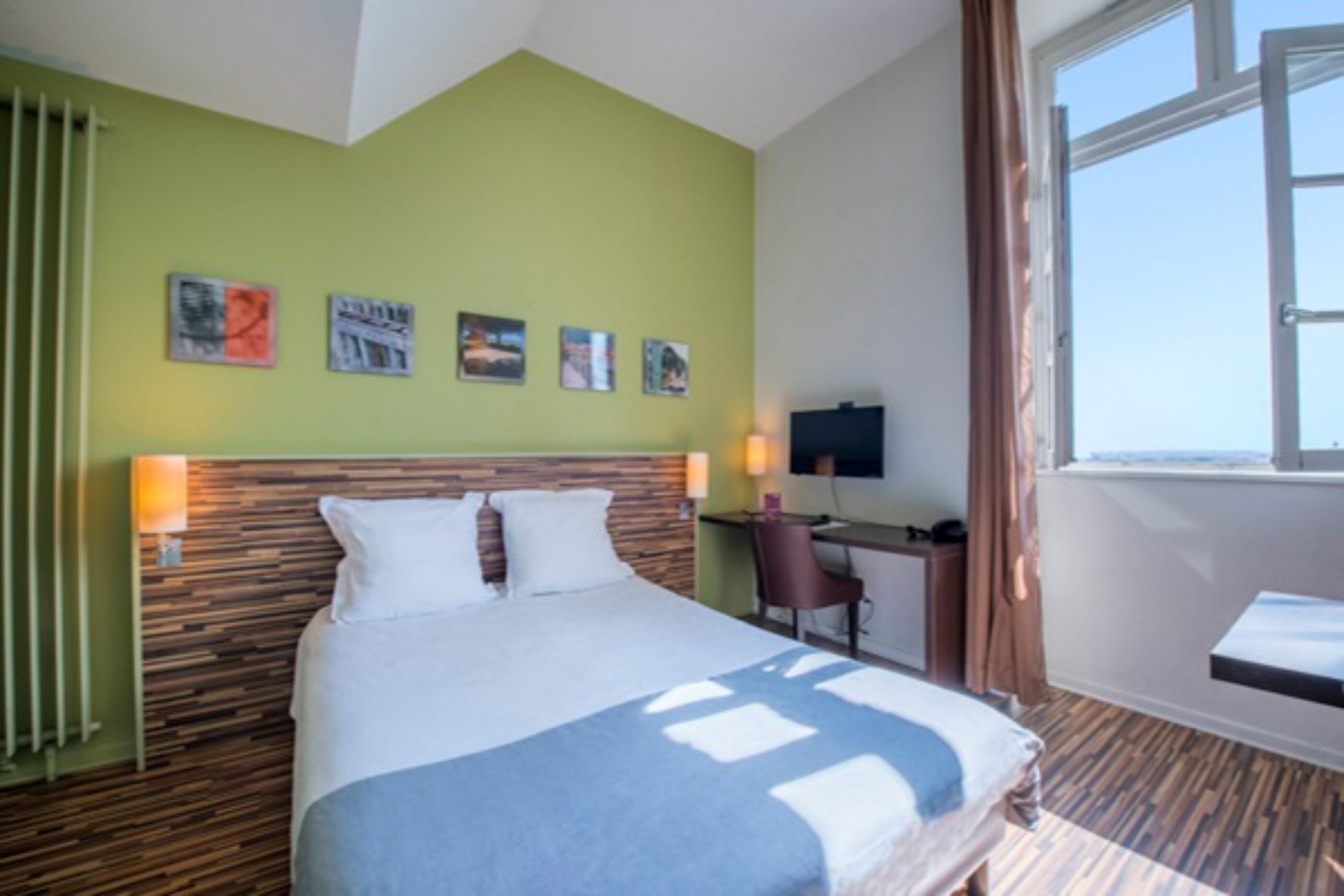 A hotel room with a bed, desk, chair, and a window with curtains.