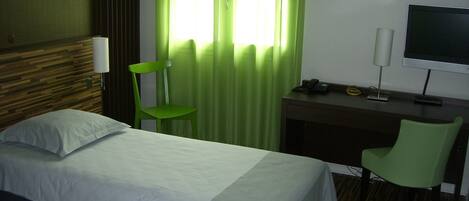Habitación de hotel con cama, escritorio con silla, televisor y ventana con cortinas verdes.