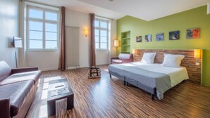 Habitación de hotel con cama, sofá, mesita de centro y ventana con cortinas.