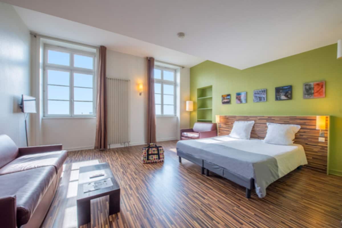 A hotel room with a bed, a sofa, a coffee table, and a window with curtains.