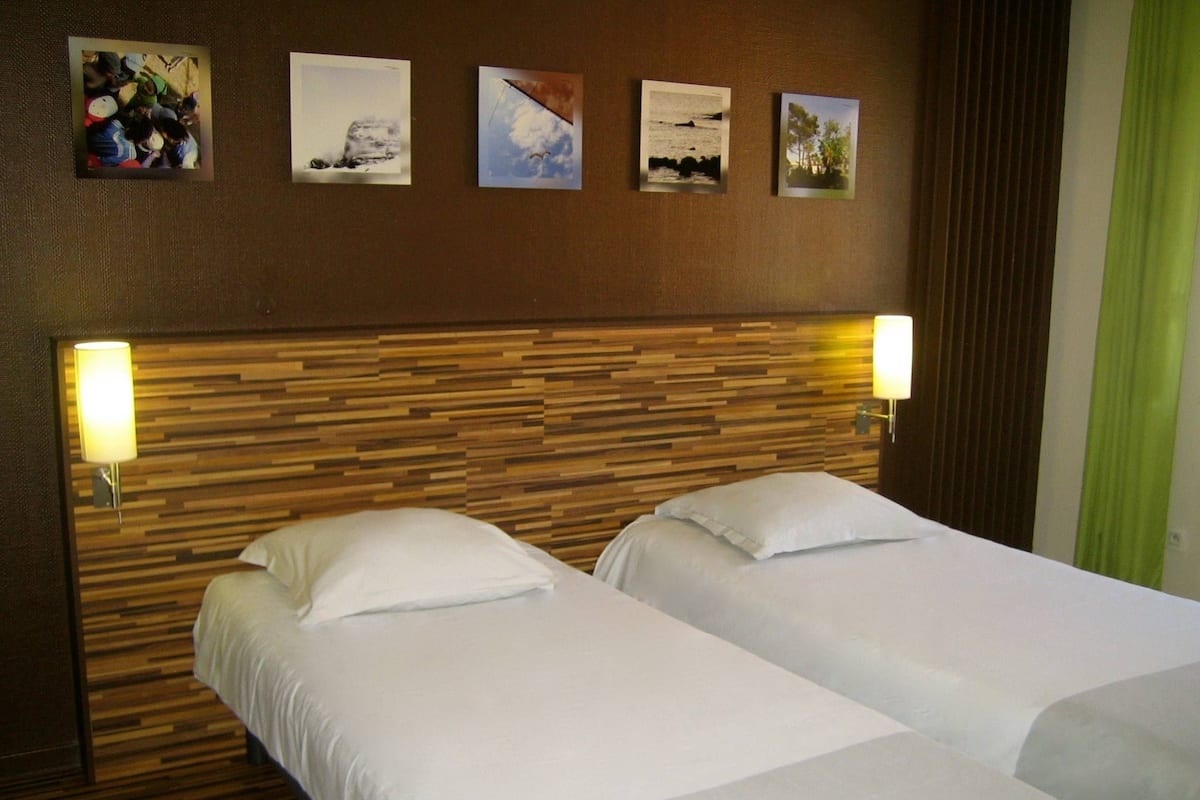 A hotel room with two beds, wooden headboard, and four framed pictures on the wall.