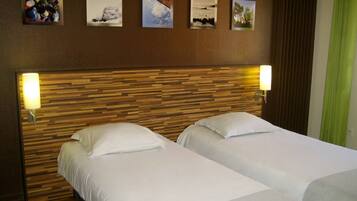 Ein Hotelzimmer mit zwei Betten, einem Holzkopfende und vier gerahmten Bildern an der Wand.
