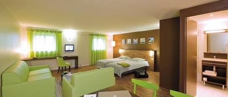 A hotel room with a bed, a desk, a laptop, a TV, and a seating area with chairs.