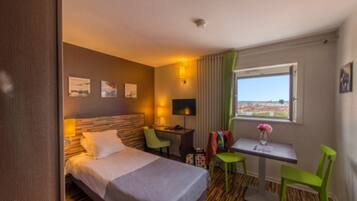 Ein Hotelzimmer mit Bett, Schreibtisch, zwei Stühlen, einem kleinen Tisch mit Vase und einem Fenster mit Blick.