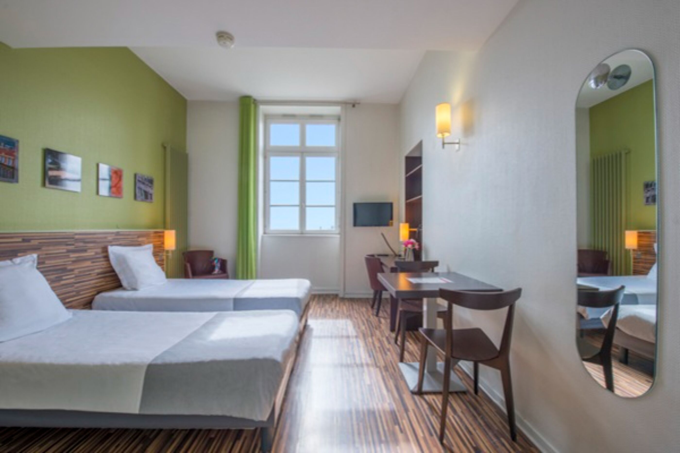 Una habitación de hotel con dos camas, un escritorio, una silla, un televisor y un espejo.