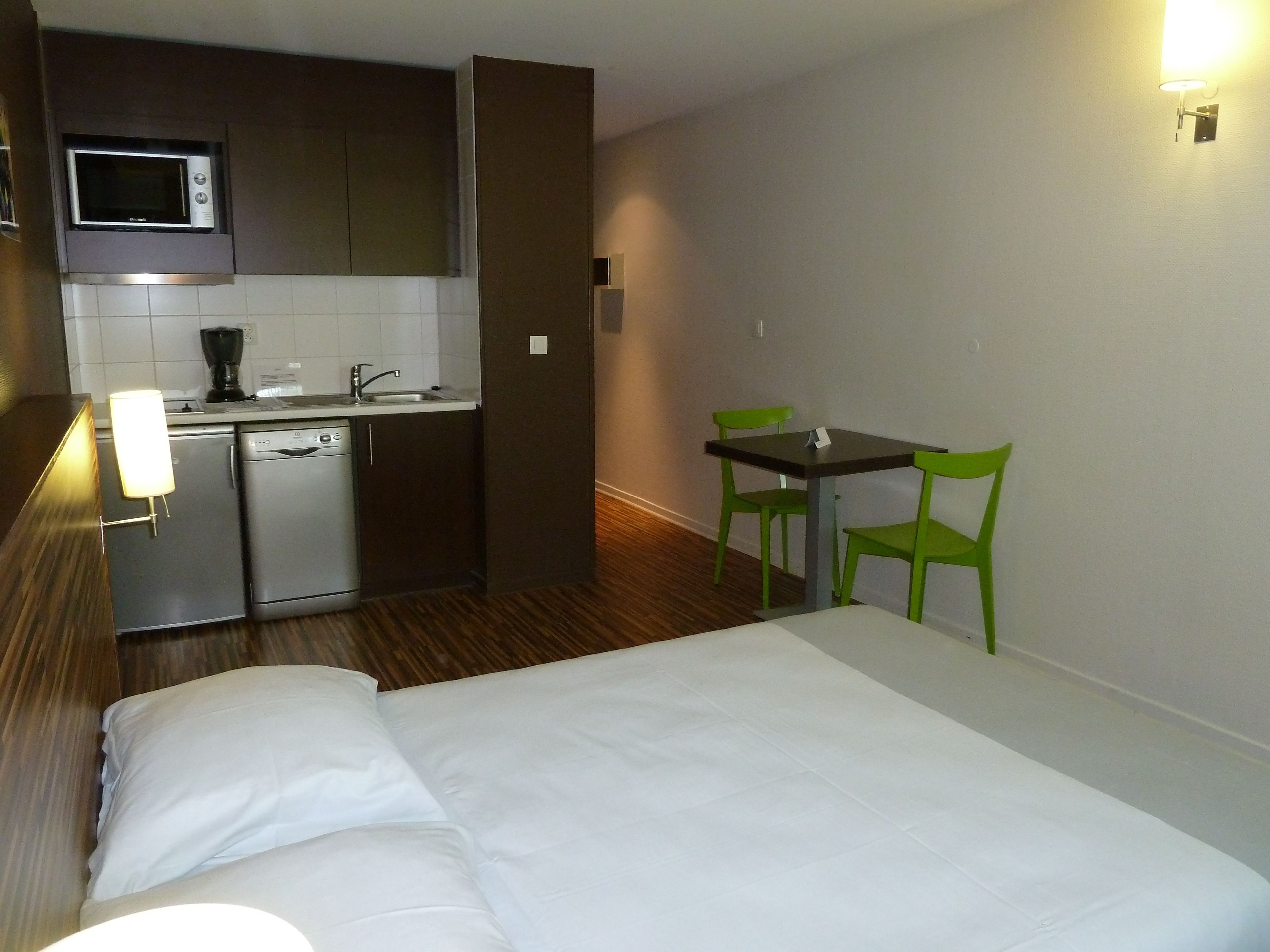 A compact hotel room with a kitchenette, a bed, and a small dining area.