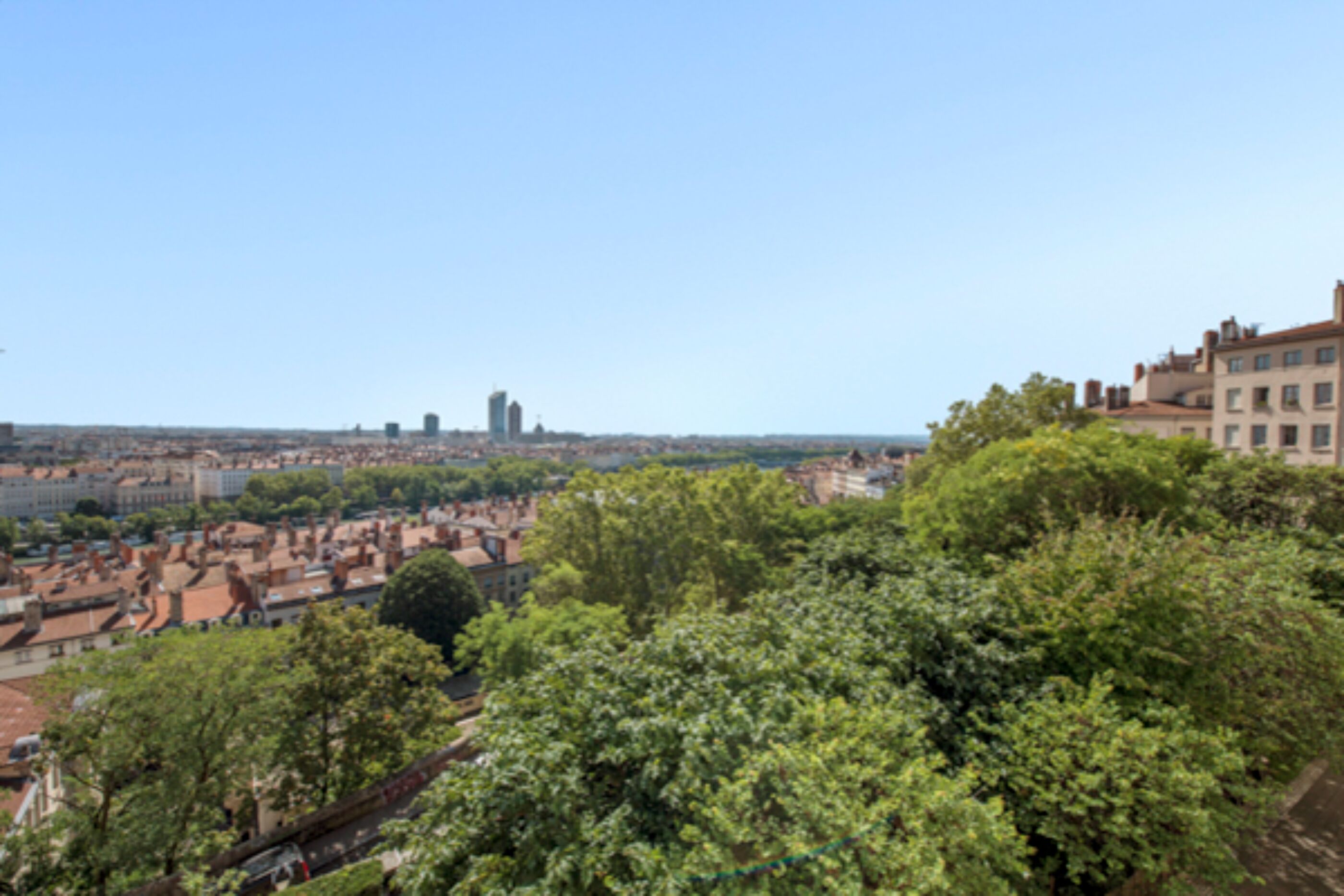 A cityscape with a mix of residential and commercial buildings, a prominent tower, and lush green trees.