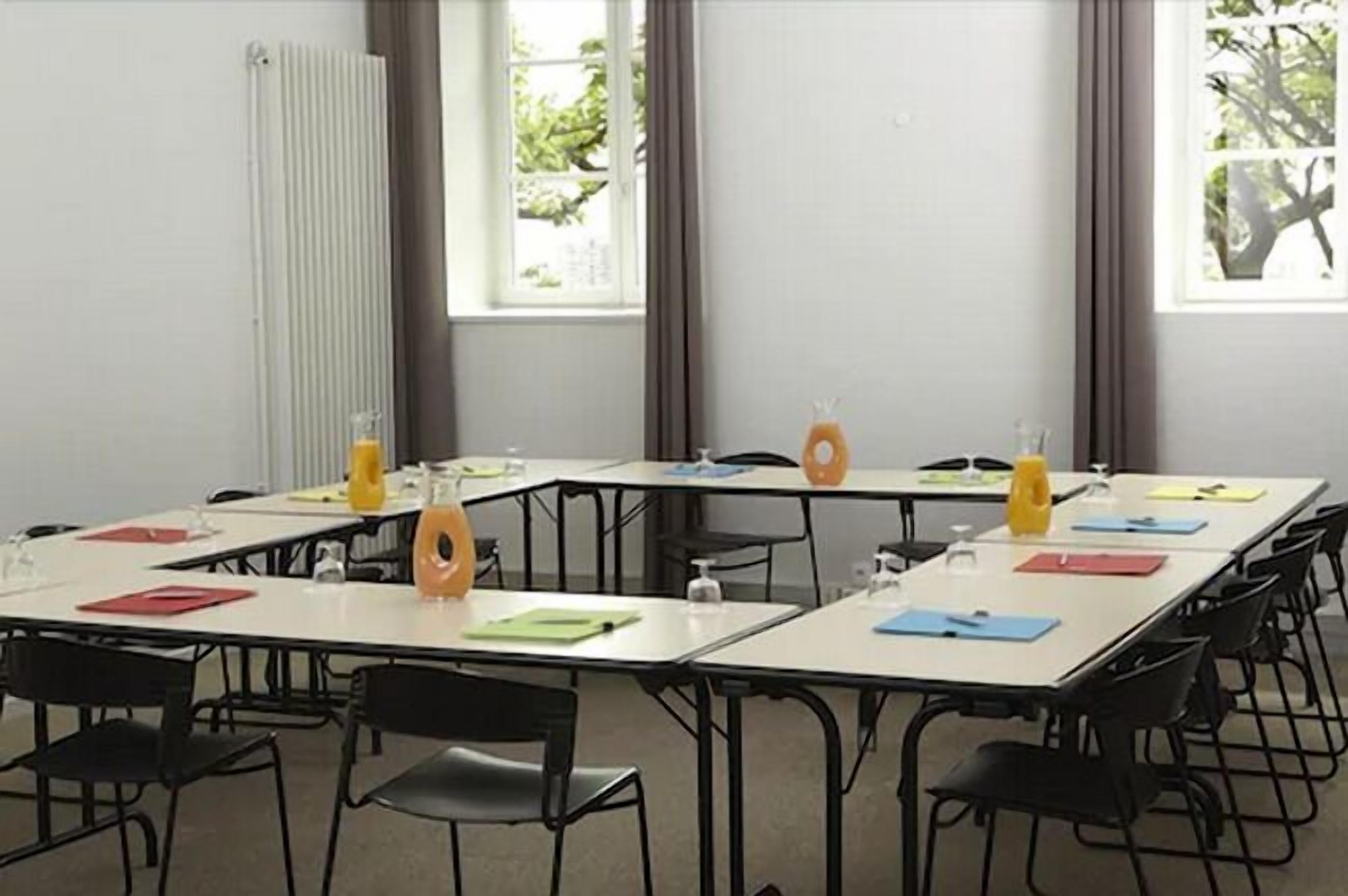 A conference room with white tables, black chairs, and large windows with curtains.