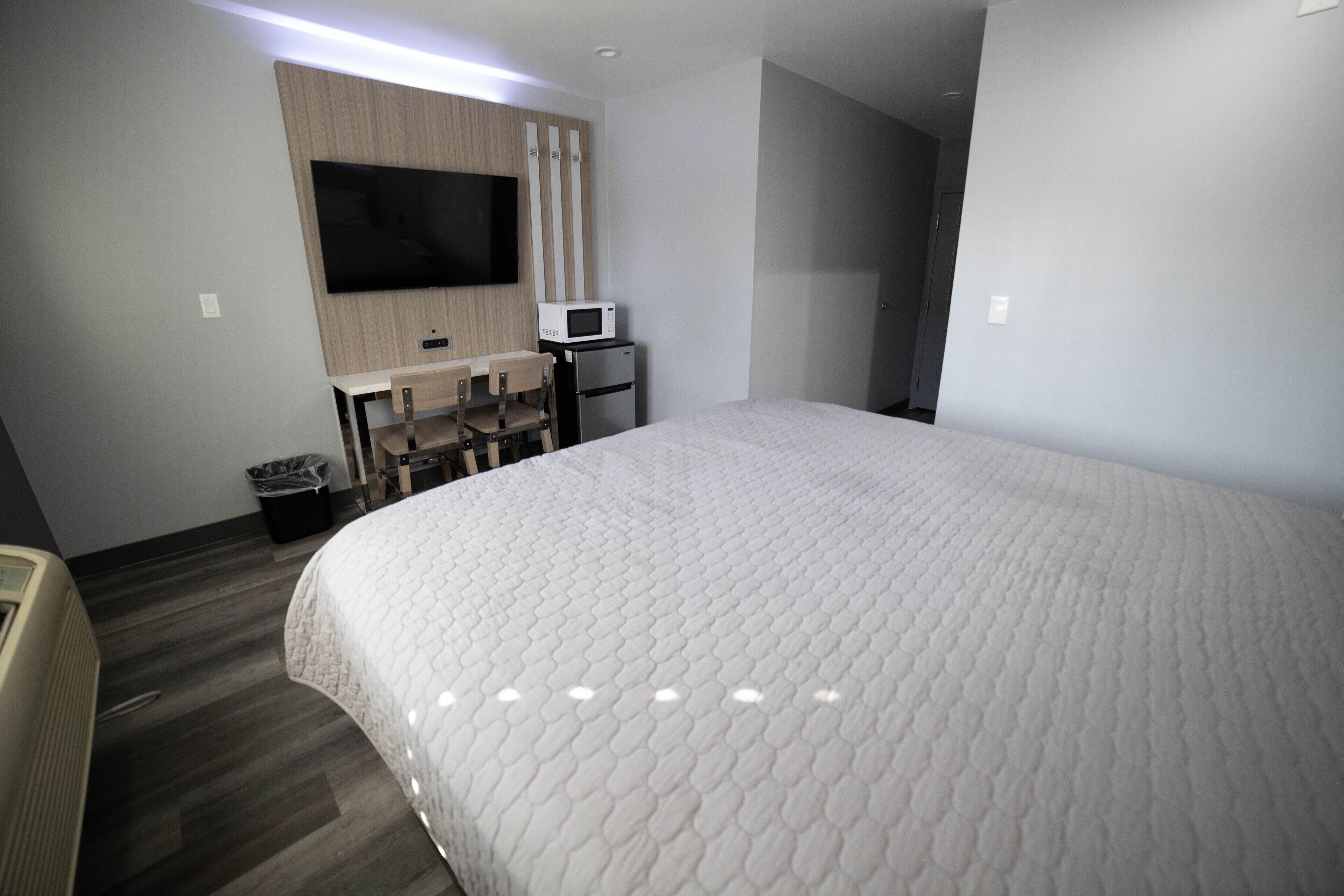 Une chambre d’hôtel dotée d’un grand lit, d’un téléviseur à écran plat fixé au mur, d’un four à micro-ondes, d’un petit réfrigérateur et d’un bureau avec deux chaises.