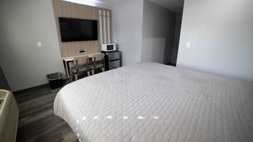 Une chambre d’hôtel dotée d’un grand lit, d’un téléviseur à écran plat fixé au mur, d’un four à micro-ondes, d’un petit réfrigérateur et d’un bureau avec deux chaises.