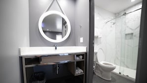 Une salle de bain moderne avec un mur en marbre gris, un lavabo blanc avec un miroir au-dessus, des toilettes et une douche à parois de verre.