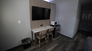 Une petite cuisine équipée d’un micro-ondes, d’un téléviseur fixé au mur, d’une table en bois avec des chaises et d’une poubelle.