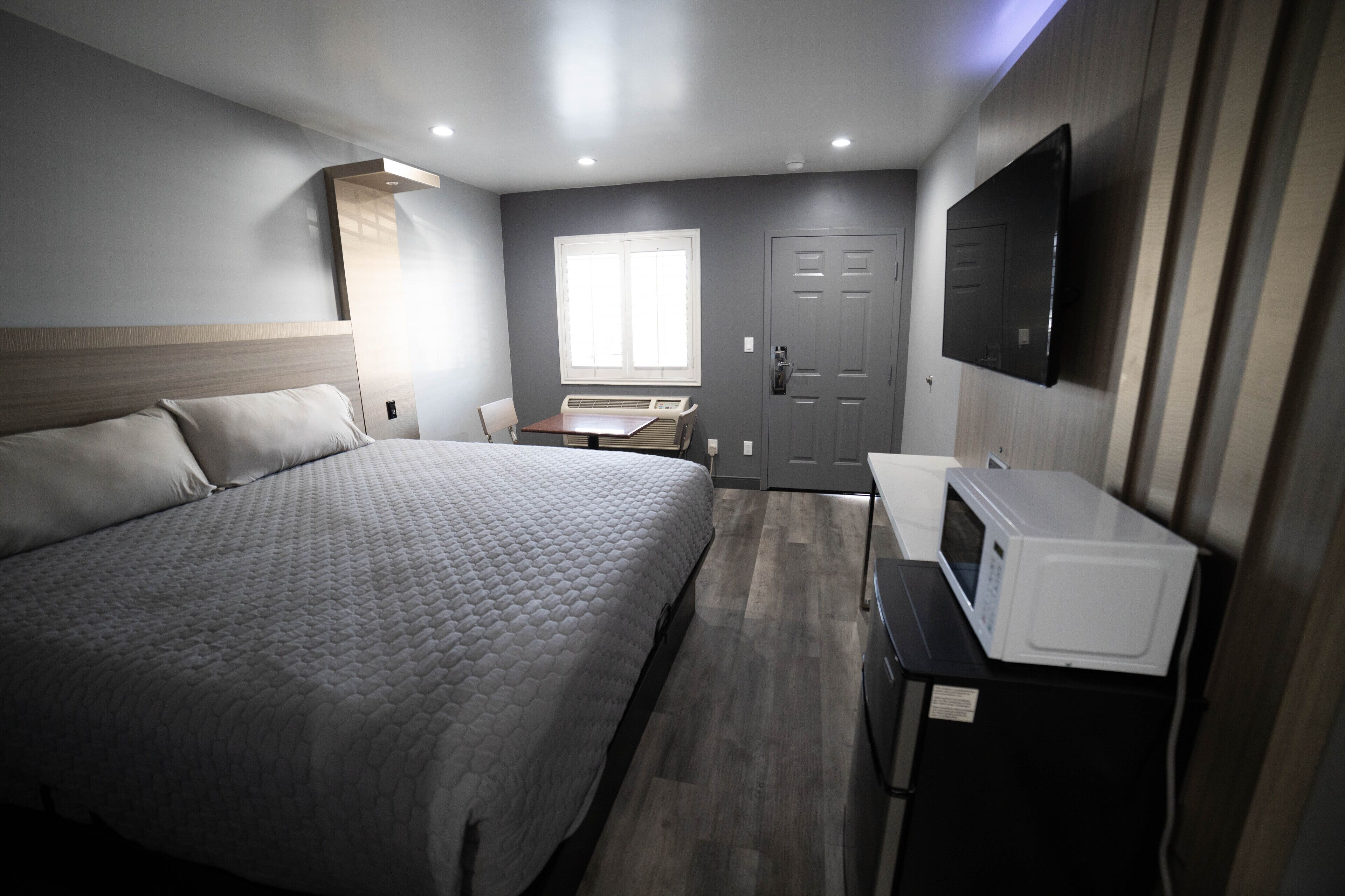 Une chambre d’hôtel avec un grand lit, un téléviseur à écran plat fixé au mur, un four à micro-ondes posé sur un plan de travail et une fenêtre avec des stores.