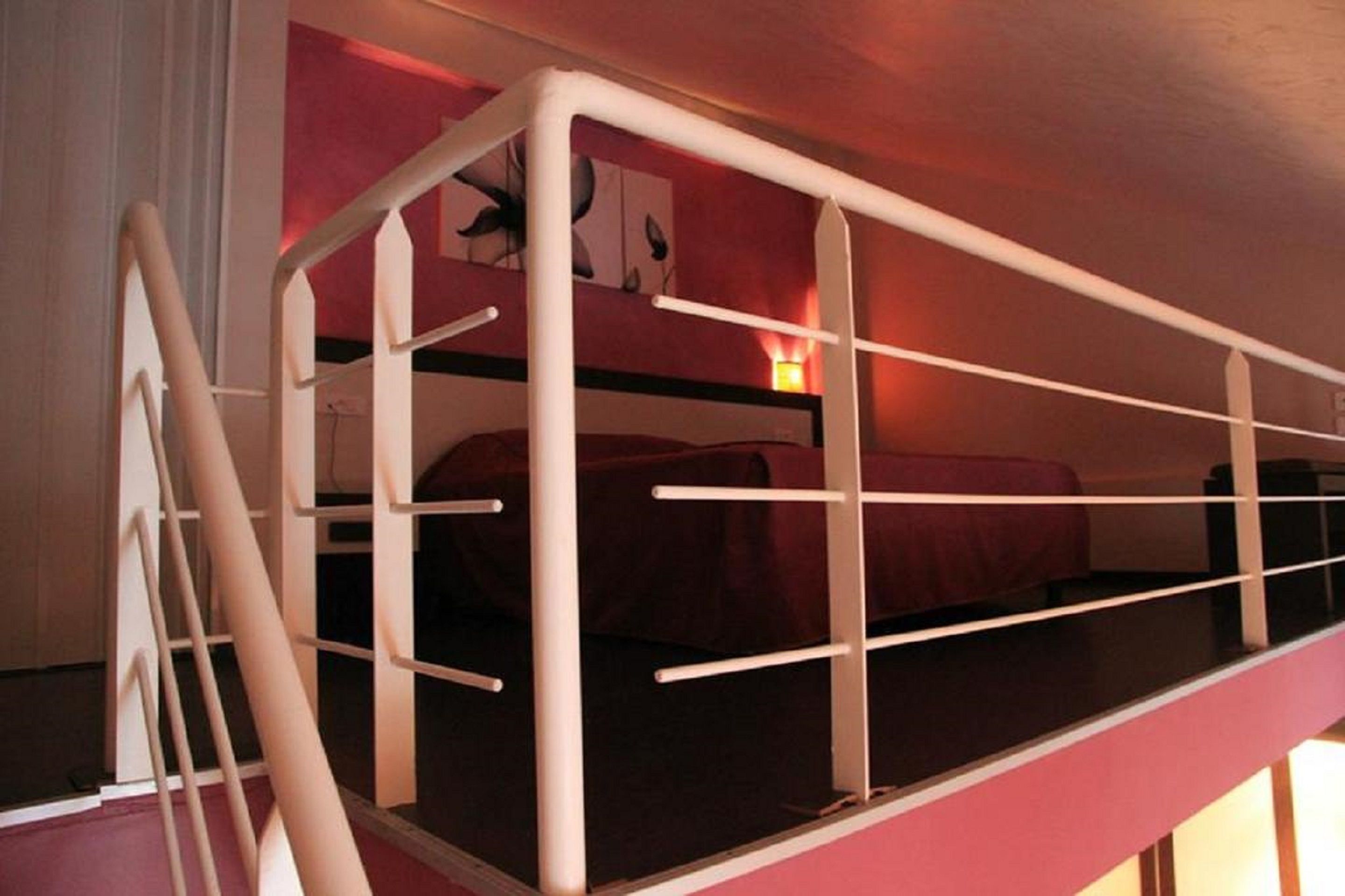 A bunk bed with a ladder, a red bedspread, and a wall-mounted light.
