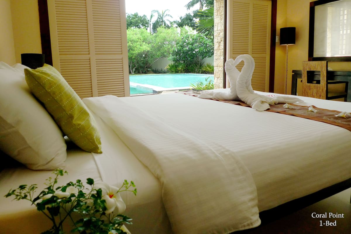 A 1-bed room with a bed, pillows, a view of a pool, and a TV.