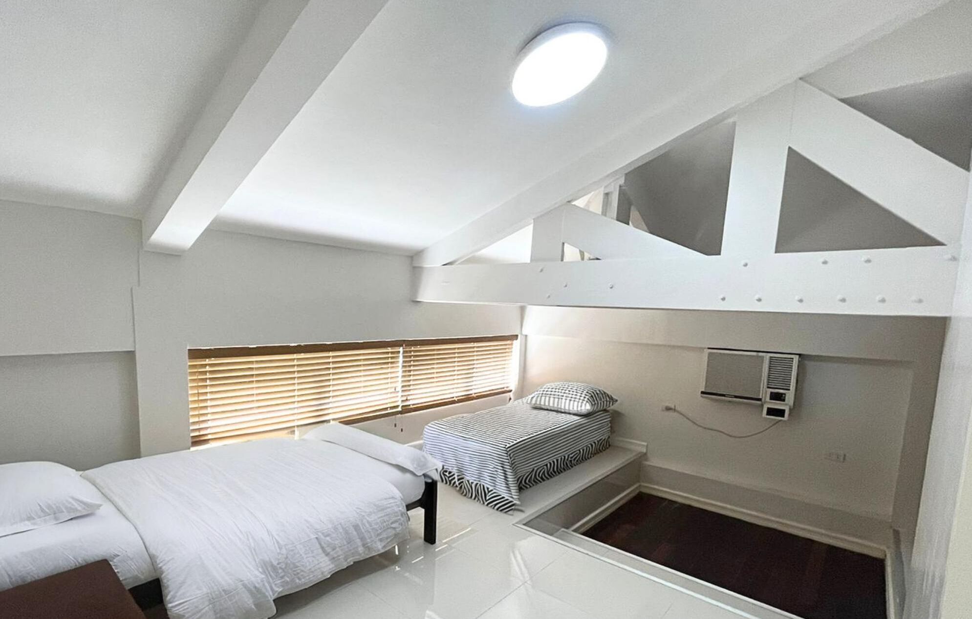 A compact, modern room with a bunk bed, a small bedside table, and a window with blinds.