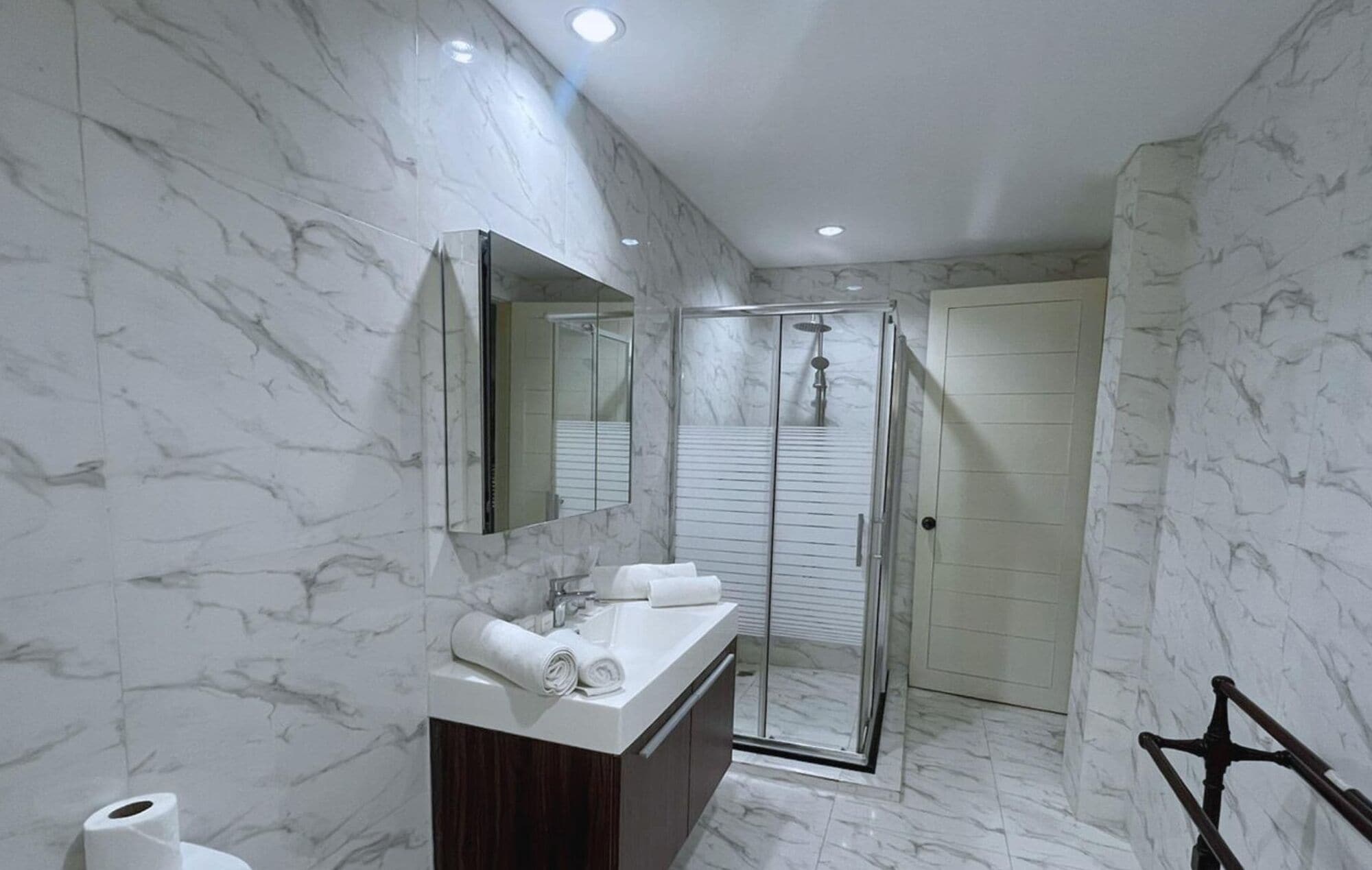 Een moderne badkamer met marmeren wanden, een glazen douchecabine en een houten wastafelmeubel.