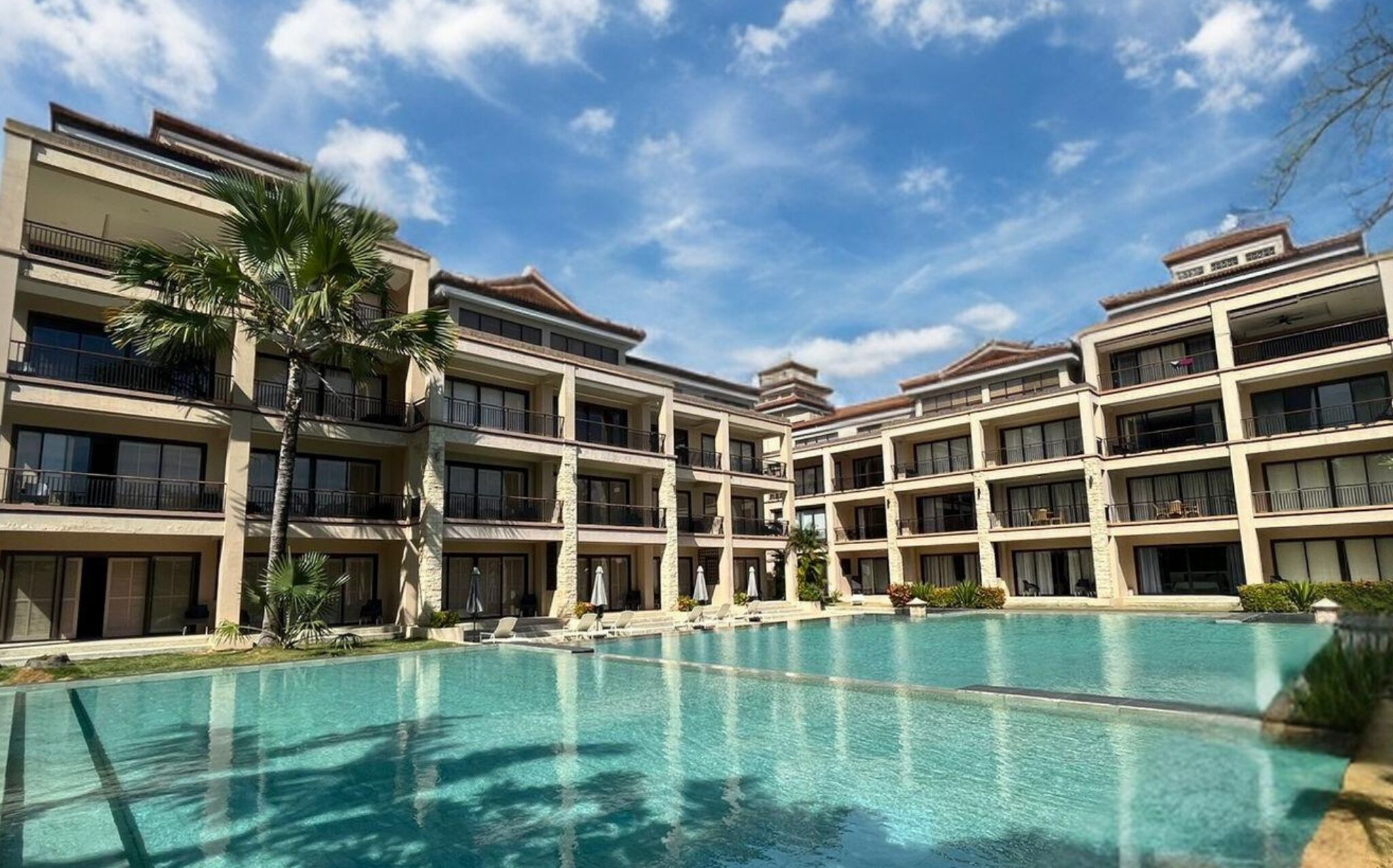 A hotel with a large pool, multiple balconies, and a clear blue sky.