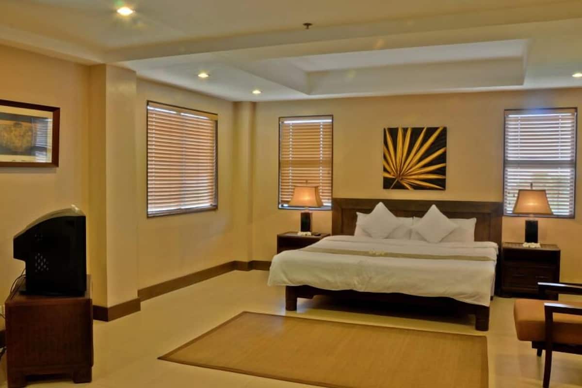 A hotel room with a large bed, two bedside tables with lamps, a television on a stand, and a painting on the wall.