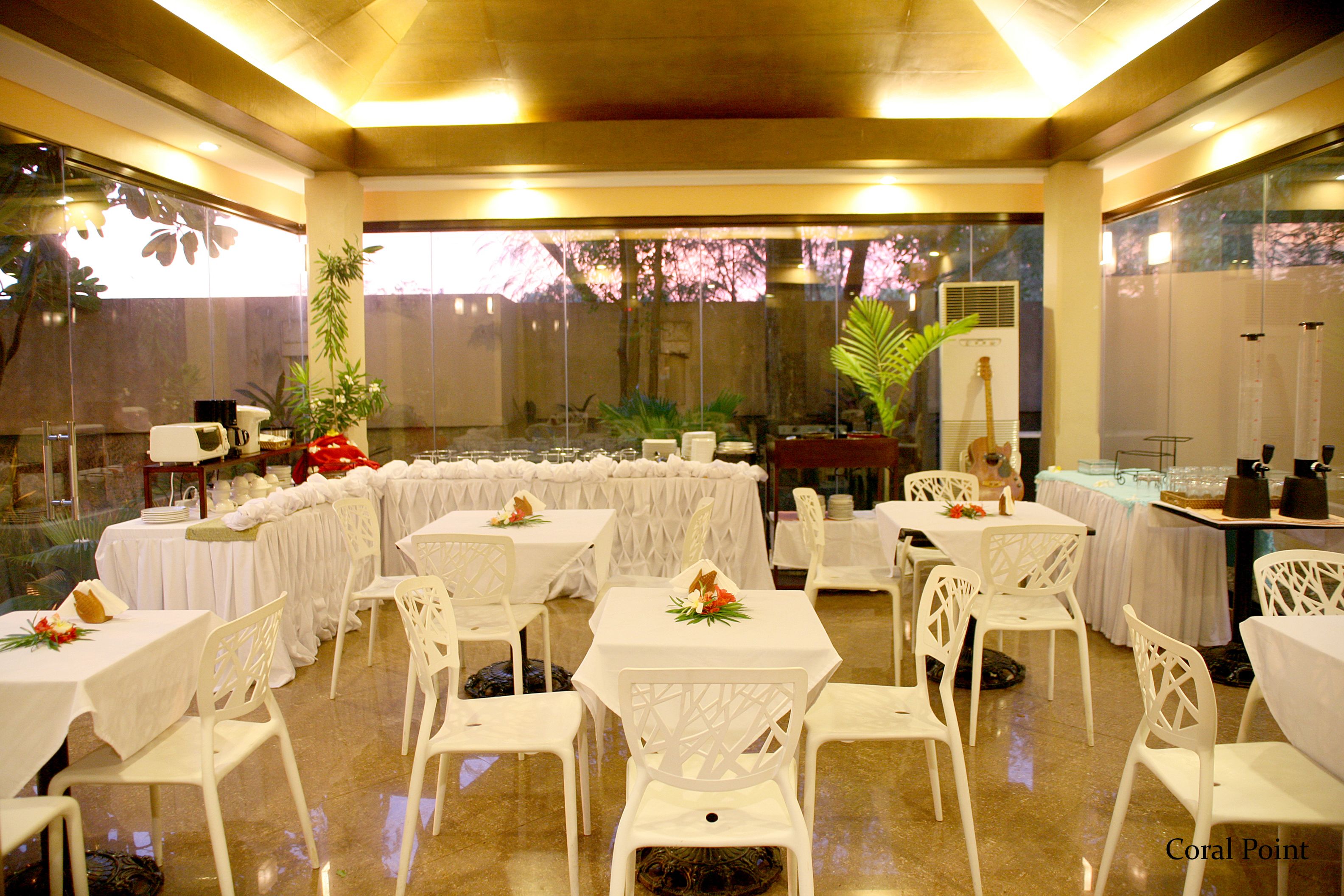 Un salón de banquetes con mesas y sillas blancas, dispuesto para un evento formal.