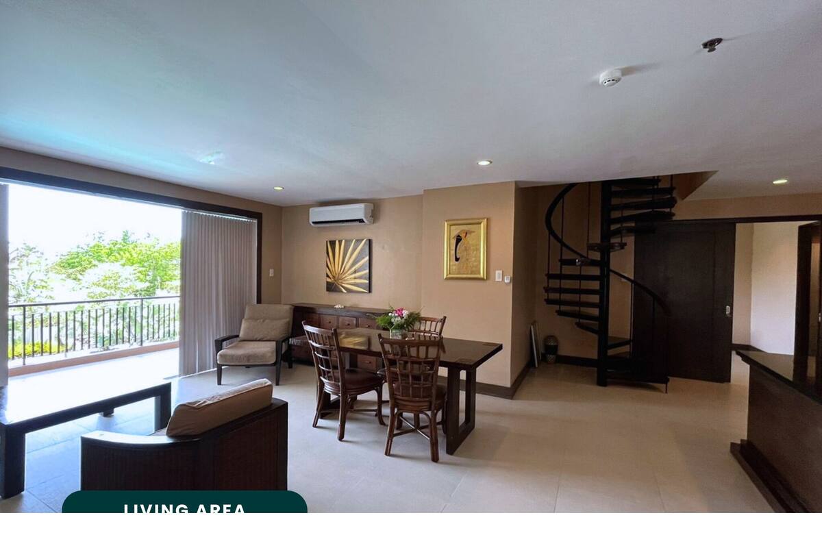 A living area with a dining table, chairs, a sofa, a staircase, and a balcony with a view.