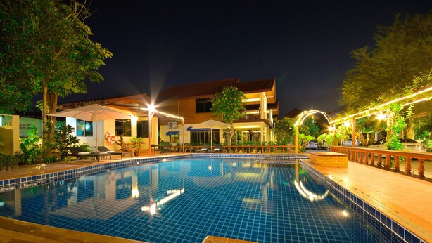 A swimming pool with tiled edges, surrounded by lounge chairs and umbrellas, and a building with a tiled roof in the background. - Avila Resort (Pattaya)