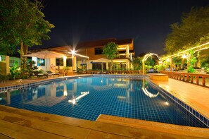 A swimming pool with tiled edges, surrounded by lounge chairs and umbrellas, and a building with a tiled roof in the background. - Avila Resort (Pattaya)