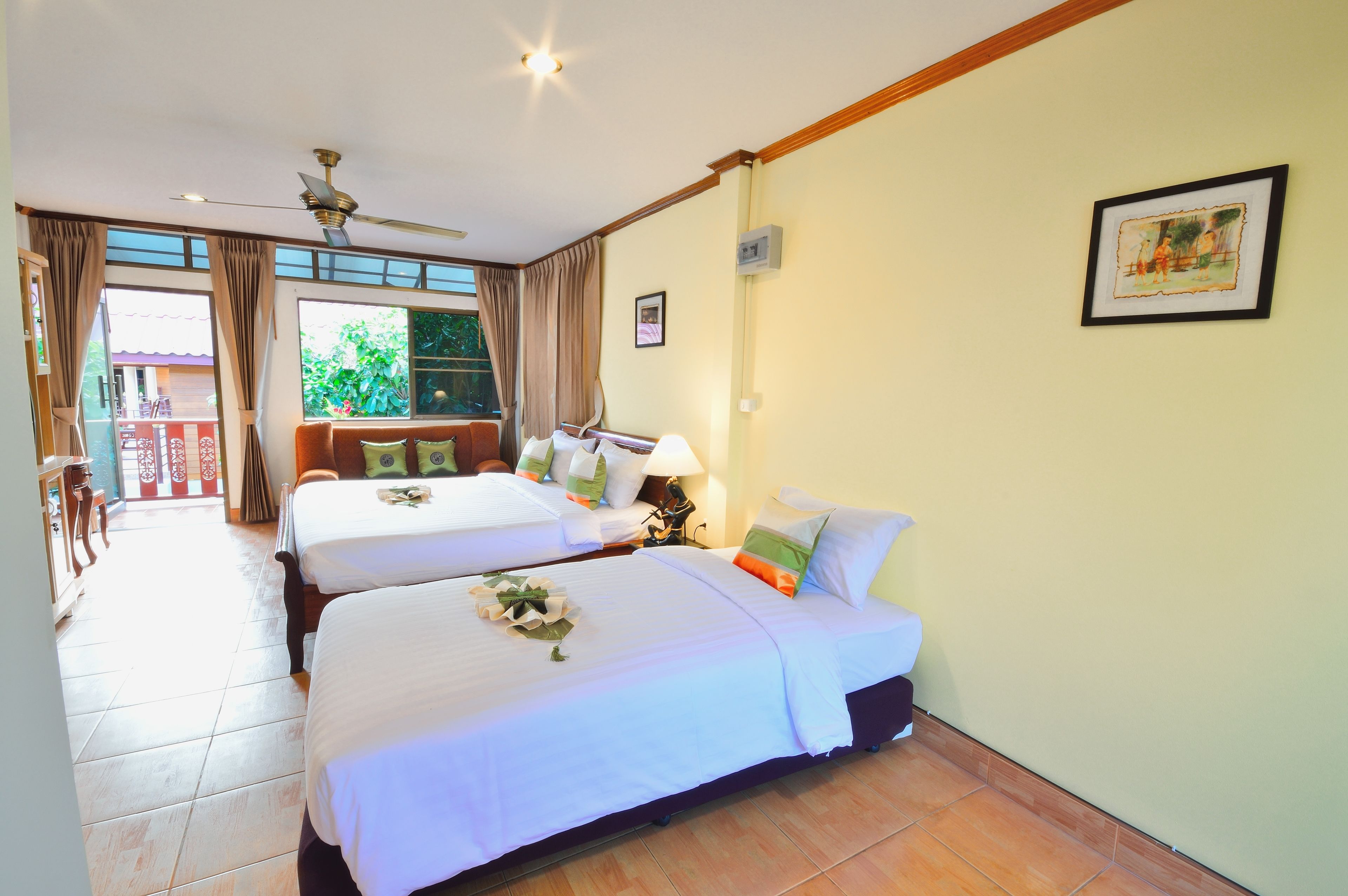 Habitación de hotel con dos camas, ventilador de techo, ventana con cortinas e imagen enmarcada en la pared.