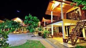 A hotel with multiple levels, outdoor seating areas, and a well-lit entrance. - Avila Resort (Pattaya)