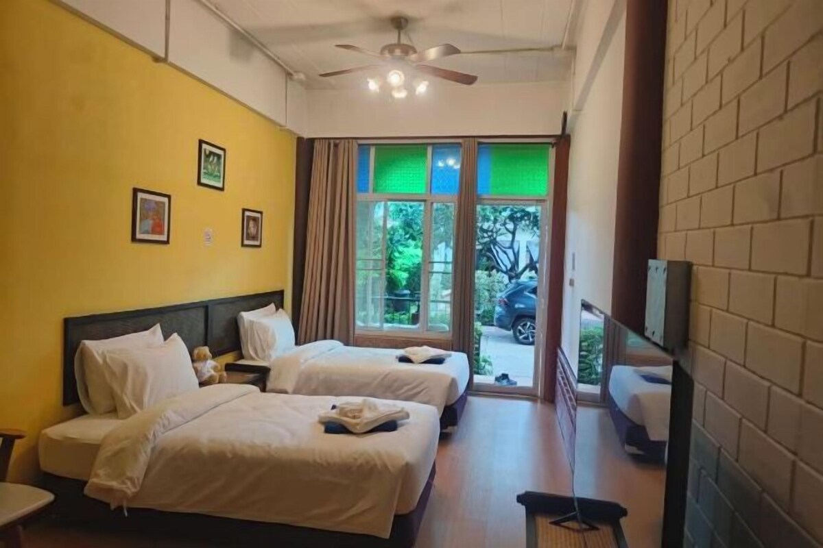 A hotel room with two beds, a ceiling fan, a television, and a view of the outdoors.