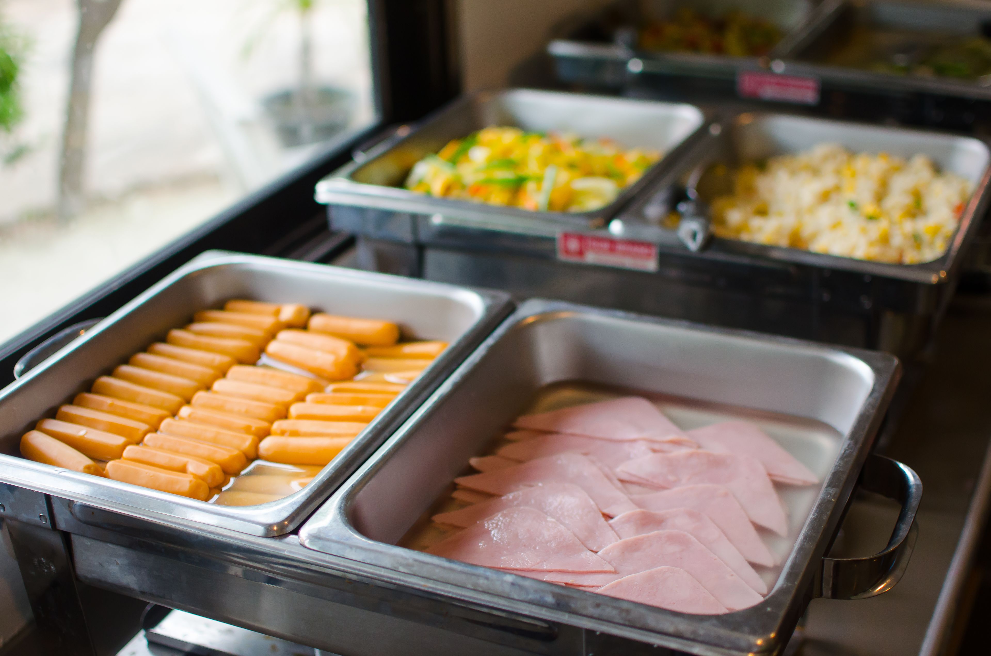 A buffet with various food items including hot dogs, ham, and other dishes.