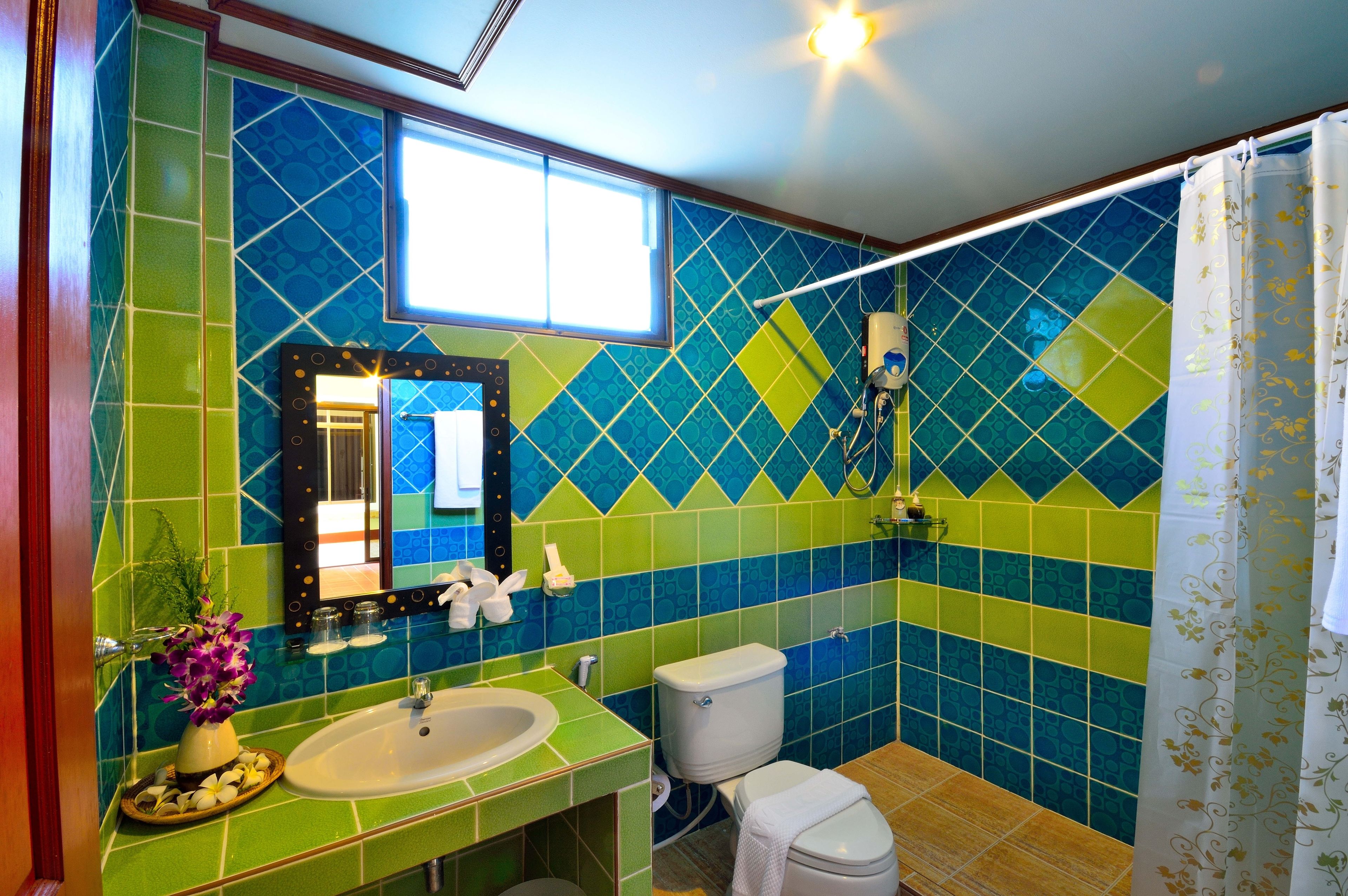 Ein Badezimmer mit einer Wand aus grün-blauen Fliesen, einem Waschbecken, einer Toilette und einer Duschvorhang.