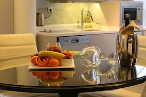 A modern kitchen with a glass dining table, a bowl of fruit, and a wine glass.