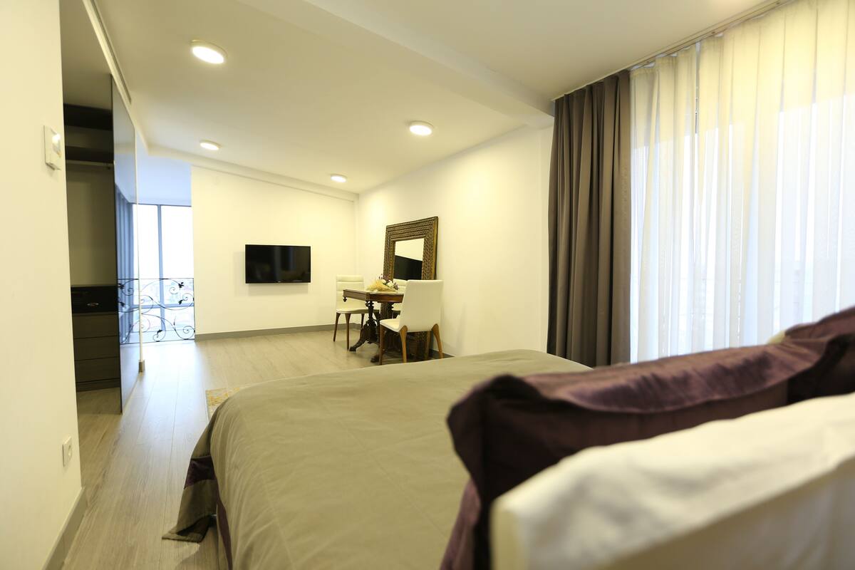 A hotel room with a bed, a desk with a chair, a television, and a window with curtains.