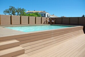 A wooden deck with a swimming pool, wooden fence, and a chair. - Aparthotel Arrels d'Empordà (Palafrugell)