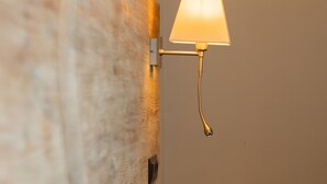 Un lit bien fait, avec du linge de lit blanc, une tête de lit en bois et une lampe fixée au mur.