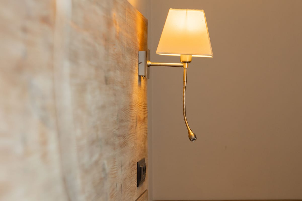 Un lit bien fait, avec du linge de lit blanc, une tête de lit en bois et une lampe fixée au mur.