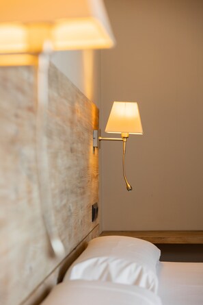 Una cama bien hecha con sábanas blancas, un cabecero de madera y una lámpara de pared.