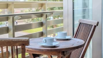 Un balcon avec une table et des chaises en bois, deux tasses blanches et une fenêtre en verre.