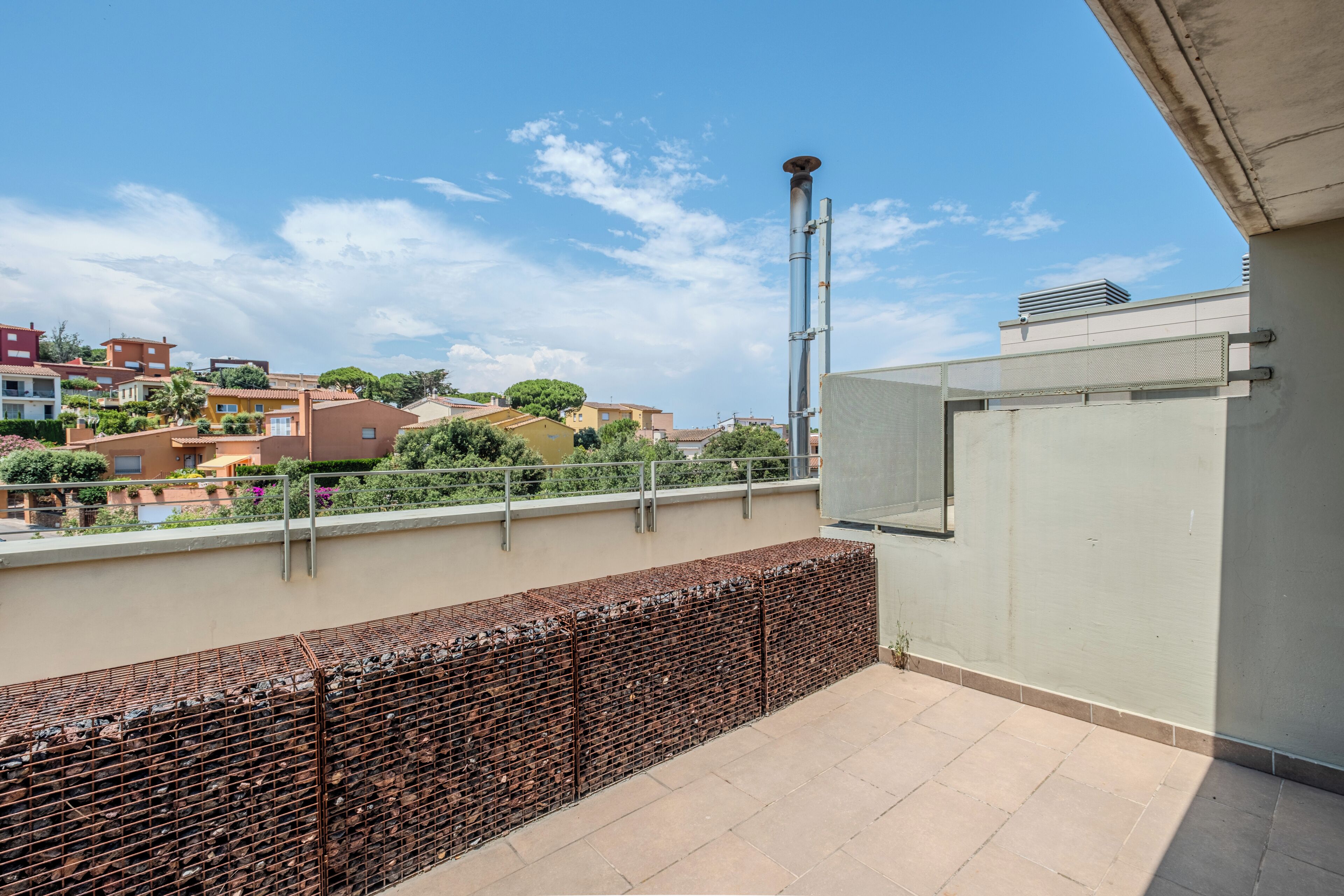 Una terraza en la azotea con barandilla de metal, vista panorámica de la ciudad y cielo despejado.