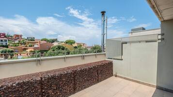 Una terraza en la azotea con barandilla de metal, vista panorámica de la ciudad y cielo despejado.